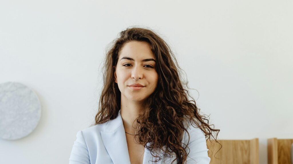 Professional woman in a white blazer standing confidently in an office with arms crossed.